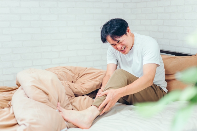 ベッドの上で足の違和感を感じる男性 | 脳活整体ルーム APLO(アプロ)