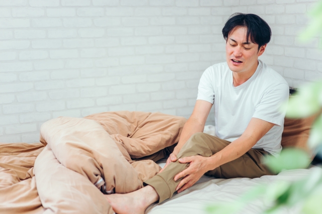 ベッドの上で足の違和感を感じる男性 | 脳活整体ルーム APLO(アプロ)